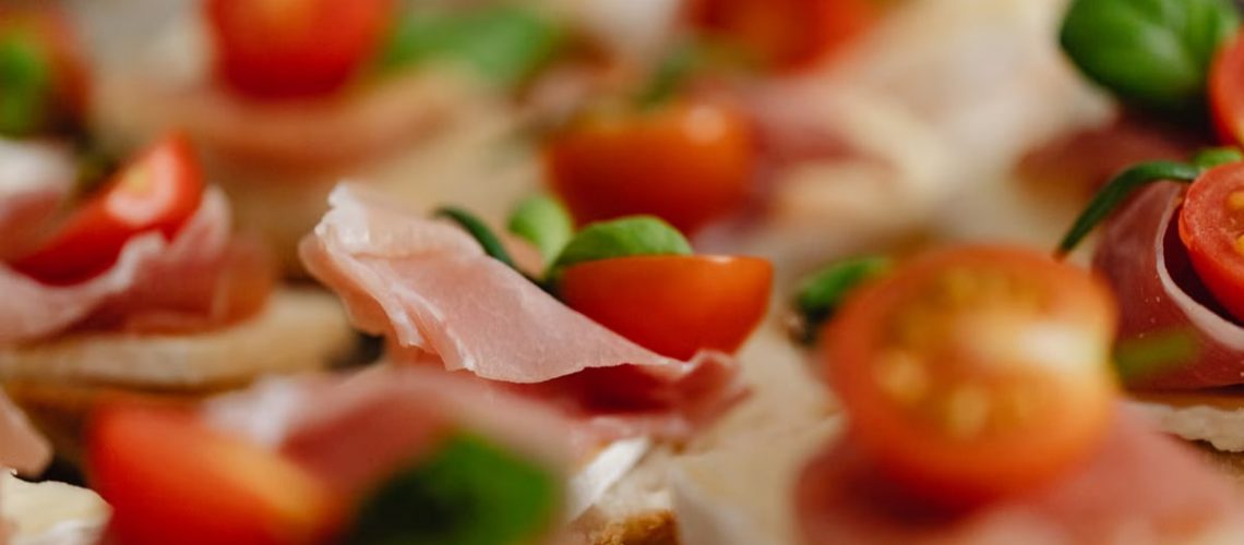 Appetizing canapes topped with prosciutto, cherry tomatoes, and fresh basil leaves.