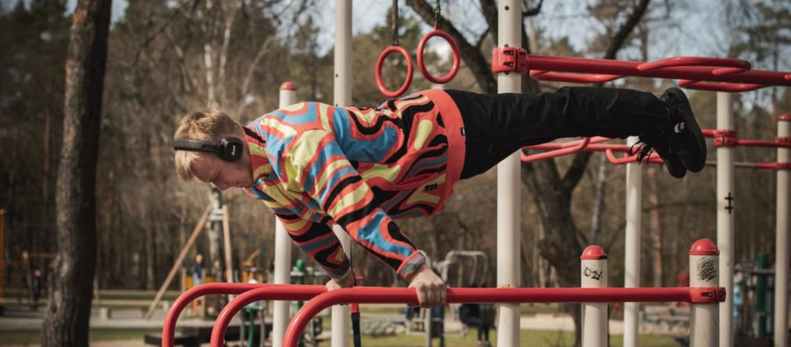 Young adult man exercises on outdoor gym bars in a colorful outfit in Vilnius, Lithuania.